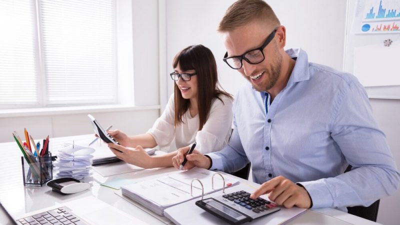 Two,Young,Businesspeople,Calculating,Invoice,With,Calculator