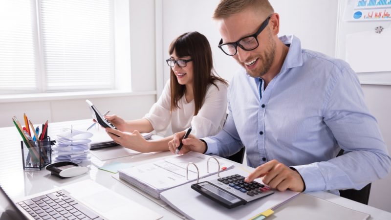 Two,Young,Businesspeople,Calculating,Invoice,With,Calculator