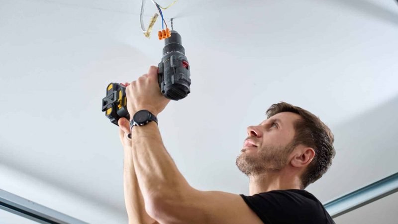 Man,Wearing,Work,Overalls,Drills,Hole,In,Ceiling,Using,Cordless